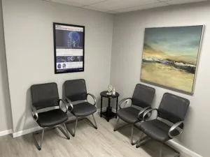 Two wall posters, four black chairs, a small round table in the waiting area of the clinic