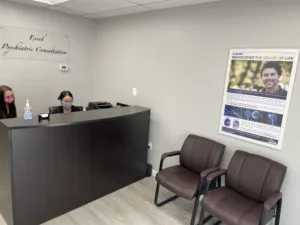 Two lady staffs in the front desk, with two brown chairs, a poster, and the clinic's logo